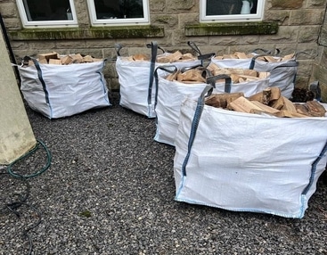 Several bags of firewood are stacked outside a house, ready for use in a fireplace or outdoor fire pit.
