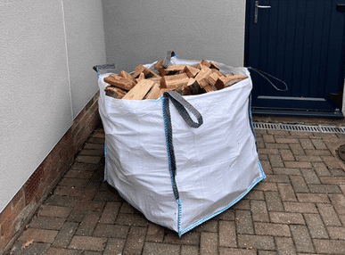 A large bag of firewood sits on the ground, freshly delivered to a customer's home for immediate use.