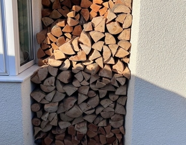 A stack of firewood logs positioned in front of a window, showcasing natural wood textures and light filtering through the glass.