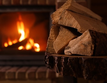 A stack of firewood rests beside a cozy fireplace, ready for use in warming the room.